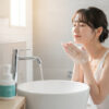 洗面台で泡を顔に当てて洗顔する女性。目を閉じ、リラックスした表情。