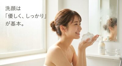 洗顔料の泡を両手に乗せた女性の笑顔。明るい浴室でのスキンケアシーン。